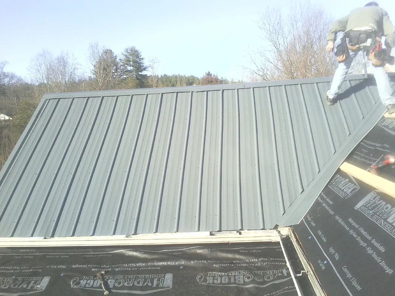 Crew installing dark green standing seam panels over synthetic underlayment in Fillmore