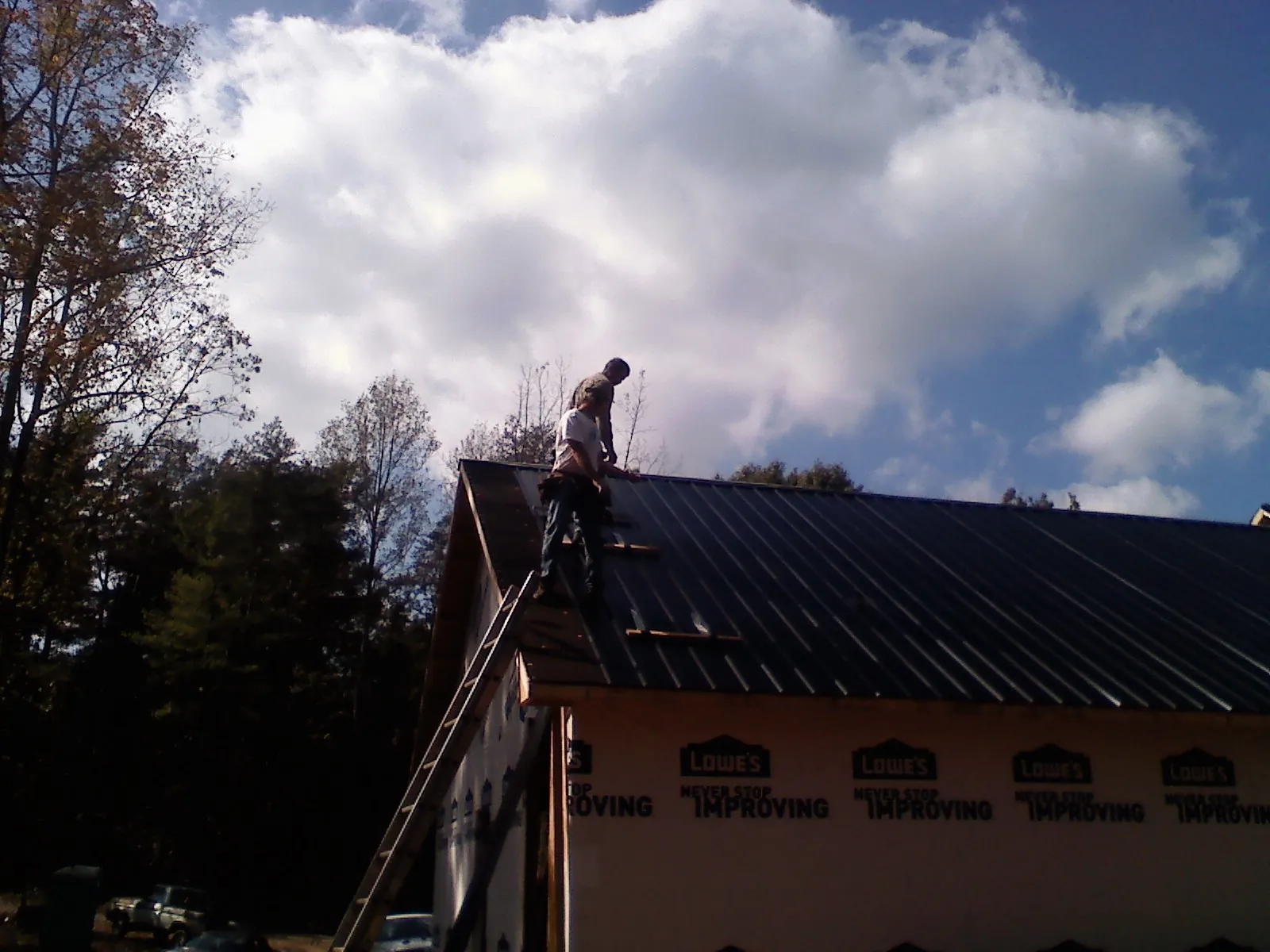 Roofer fastening dark metal panels high against a cloudy sky, from a Roof Inspection job in Fillmore