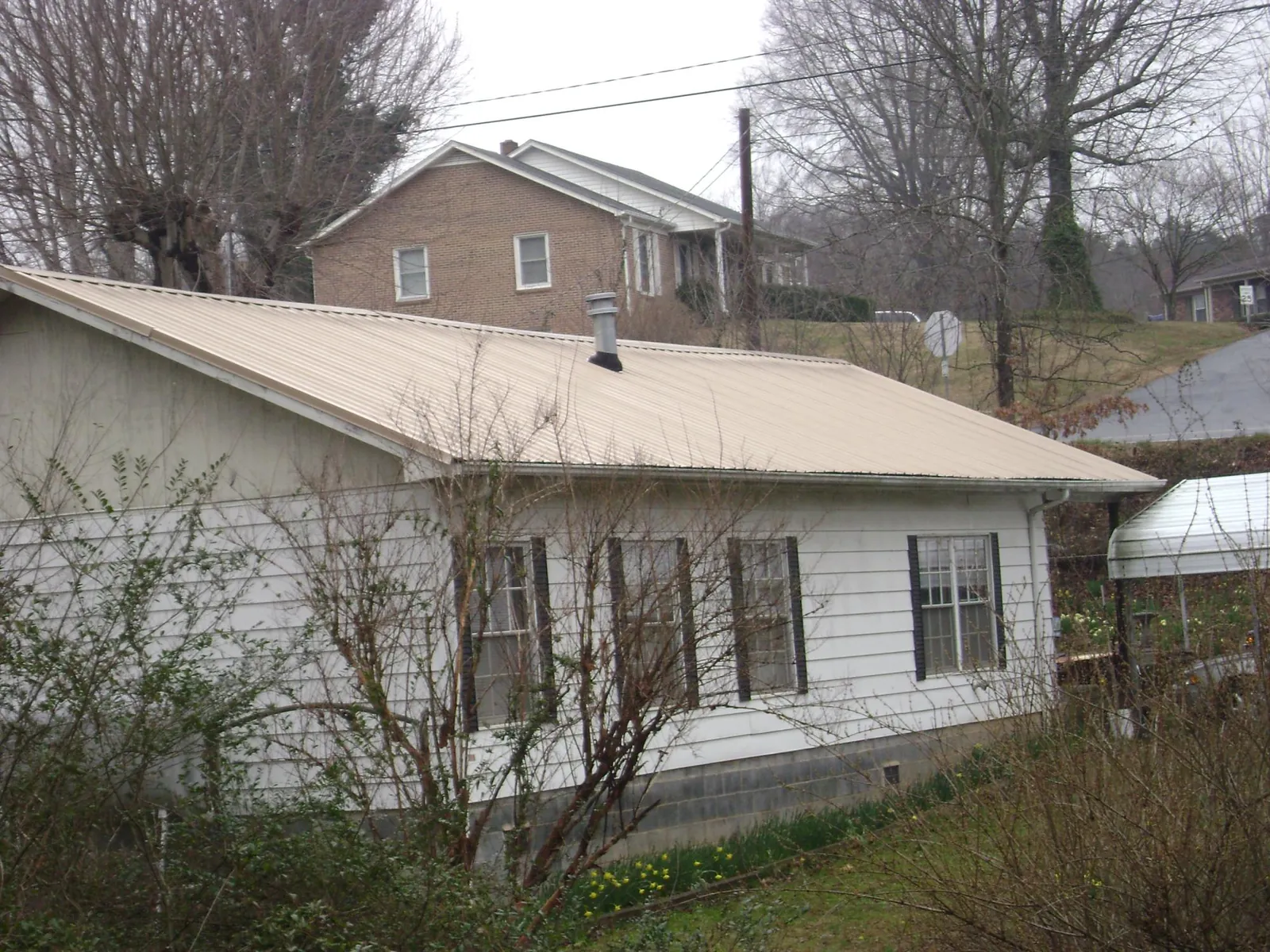 Tan metal roof on a white sided house set into a hillside — Commercial Roofing by Roofing Brothers in Fillmore